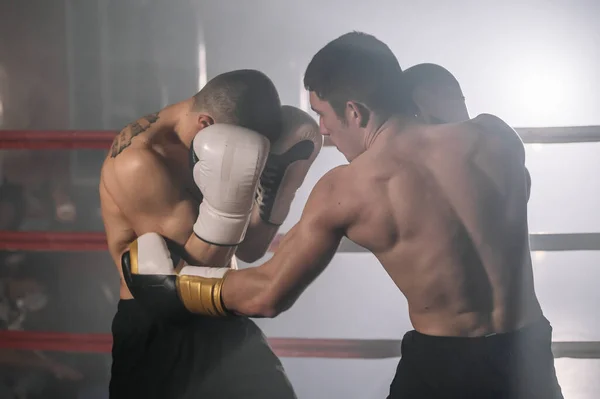 Twee professionele jonge gespierde shirtloze mannelijke boksers vechten in een boksring. — Stockfoto