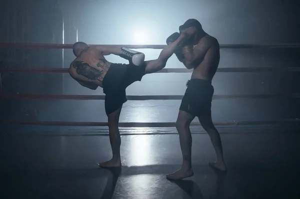 Dois homens musculosos sem camisa lutando Kick boxe combate no ringue de boxe. — Fotografia de Stock