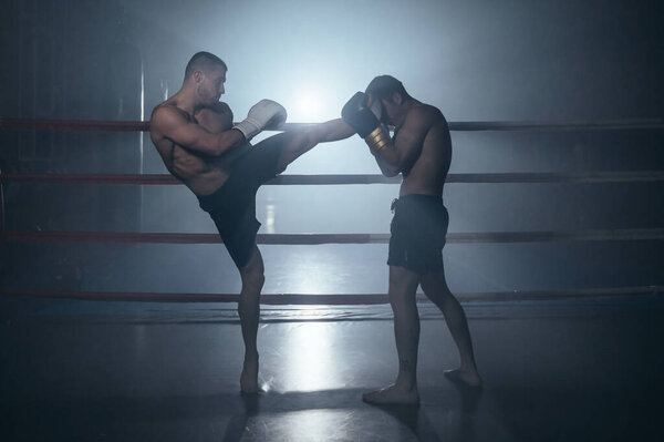 Two shirtless muscular man fighting Kick boxing combat in boxing ring.