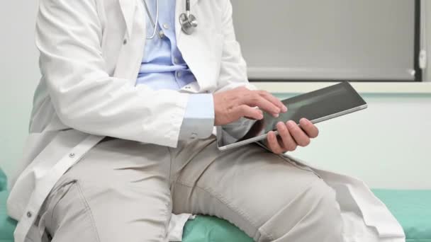 Tilt up shot of male doctor in lab coat with stethoscope using digital tablet during workday in clinic. — Vídeo de stock
