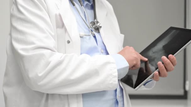 Tilt up shot of male doctor in lab coat with stethoscope using digital tablet during workday in clinic. — Stock Video