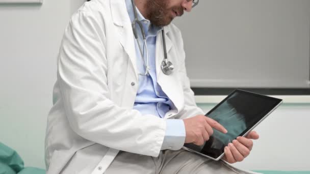 Läkaren undersöker en röntgenbild av en patient i en digital tablett på läkarmottagningen. — Stockvideo