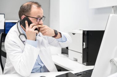 Doktor endişeli görünüyor bir masaüstü bilgisayar ekranı, Bir tıbbi muayene sonuçları kontrol.