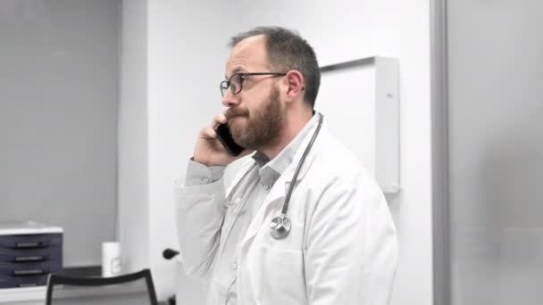 Доктор в офисе разговаривает по телефону — стоковое видео