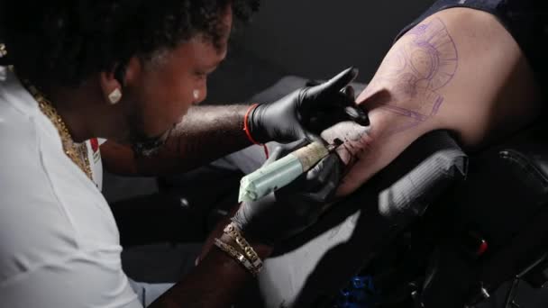 Profesional afroamericano tatuaje artista hace un tatuaje en el brazo del cliente — Vídeos de Stock