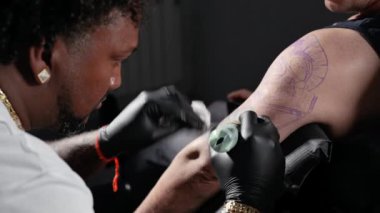 Profesyonel Afro-Amerikan dövme sanatçısı müşteri kolunda dövme yapıyor.