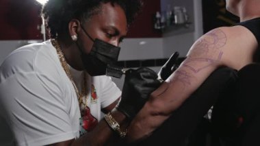 Profesyonel dövme sanatçısı genç bir adamın kolunda dövme yapıyor..