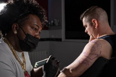 Profesyonel Afro-Amerikan dövme sanatçısı müşteri kolunda dövme yapıyor.