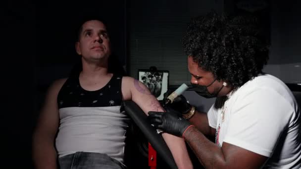 Profesional afroamericano tatuaje artista hace un tatuaje en el brazo del cliente — Vídeo de stock