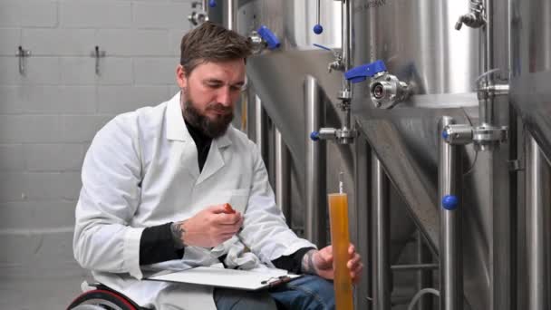 Professionele brouwmeester die het ambachtelijke bierproductieproces in de brouwerij controleert en de dichtheid van de drank meet met een hydrometer — Stockvideo