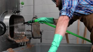 Bir bira fabrikasında çalışan erkeğin büyük paslanmaz çelik su ısıtıcısı içinde yüksek basınçlı yıkayıcı ile Temizleme.