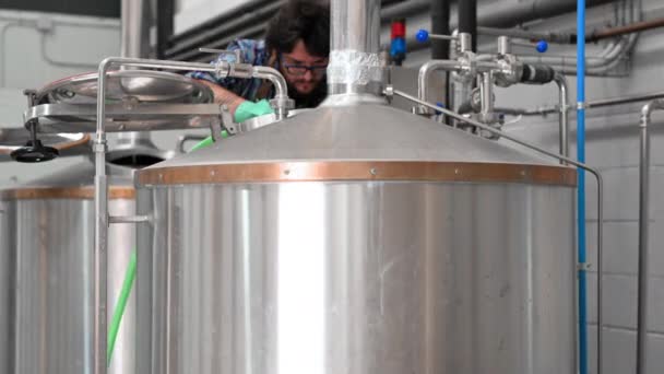 Человек, работающий на пивоваренном заводе, чистящий внутри большого чайника из нержавеющей стали с помощью мойки высокого давления . — стоковое видео