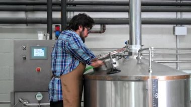 Bir bira fabrikasında çalışan erkeğin büyük paslanmaz çelik su ısıtıcısı içinde yüksek basınçlı yıkayıcı ile Temizleme.