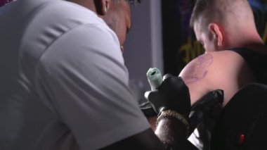 Profesyonel Afro-Amerikan dövme sanatçısı müşteri kolunda dövme yapıyor.