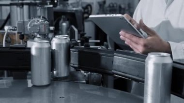 Erkek işçi, içecek fabrikası üretim hattında konserve kutularıyla taşımacılık yapan bir tablette çalışıyor. Kapatın..