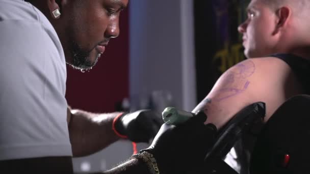 Filmagem cinematográfica em câmera lenta de um artista de tatuagem criando arte corporal no estúdio de tatuagem — Vídeo de Stock