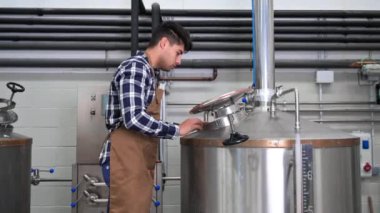 Bira fabrikasında çalışan yakışıklı bir bira imalatçısı. Arka planda metal kaplar var.