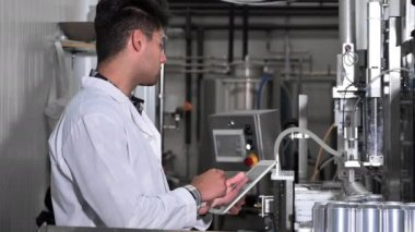 Fabrika işçisi, içecek fabrikasının üretim hattını bilgisayar tabletiyle inceliyor..