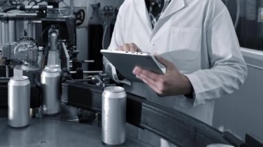 Fabrika işçisi, içecek fabrikasının üretim hattını bilgisayar tabletiyle inceliyor..