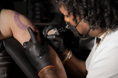 Profesyonel Afro-Amerikan dövme sanatçısı müşteri kolunda dövme yapıyor.
