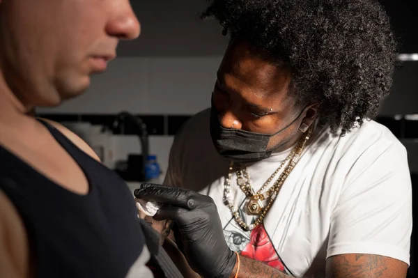Profesyonel Afro-Amerikan dövme sanatçısı müşteri kolunda dövme yapıyor.
