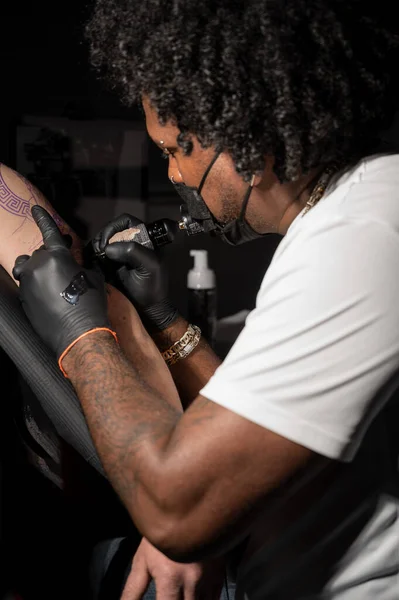 Profesional afroamericano tatuaje artista hace un tatuaje en el brazo del cliente — Foto de Stock
