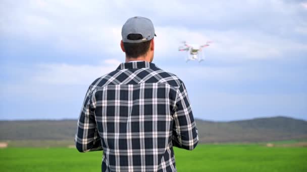 Κοντινό πλάνο του ανθρώπου αγρότη στο καπέλο στέκεται στο χωράφι με το πράσινο σιτάρι και τον έλεγχο ενός drone που φέρουν πάνω από το πεδίο. Νέες τεχνολογίες στη γεωργία. — Αρχείο Βίντεο