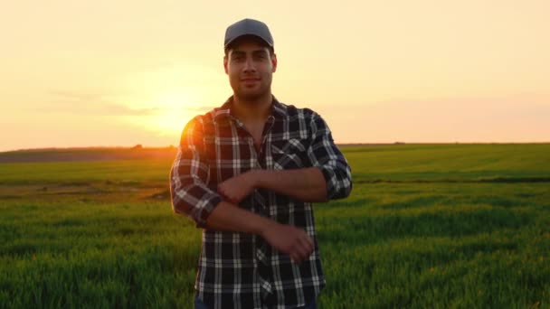 Портрет красивого молодого человека-фермера, стоящего в поле на закате, улыбающегося в камеру и скрещивающего руки. — стоковое видео