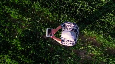 Çiftçi buğday tarlasında tablet kullanıyor. Mavi gömlekli bir çiftçinin genç bir buğday tarlasında tablet kullanışının görüntüsü. Yüksek kalite 4k görüntü