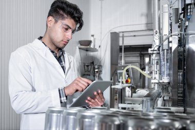 Fabrika işçisi, içecek fabrikasının üretim hattını bilgisayar tabletleriyle inceliyor. Yüksek kalite fotoğraf