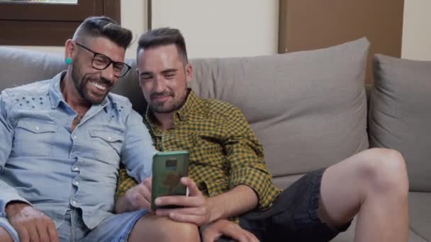 Щаслива Молода Пара Гей Використовуючи Мобільний Телефон Сидячи Дивані Вітальні — стокове відео