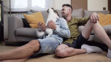 Mutlu eşcinsel çift yerde oturuyor ve evde köpekle oynuyor. Yüksek kaliteli fotoğrafçılık