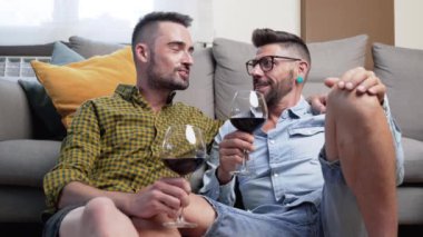 Aşık eşcinsel çift yerde oturup kırmızı şarapla kadeh kaldırıyor. Yüksek kalite 4k görüntü