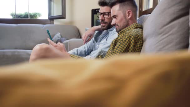Happy Young Gay Couple Using Mobile Phone While Sitting Sofa — Stok video