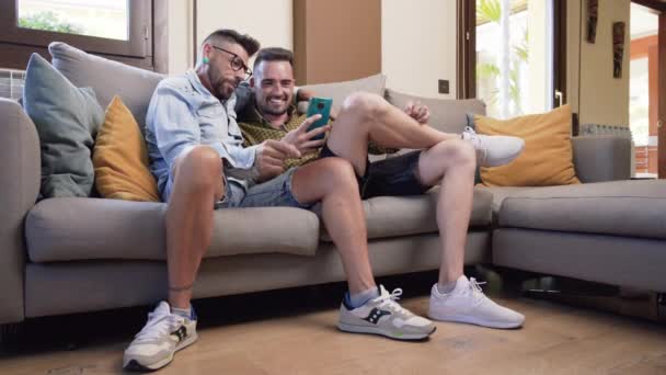 Happy Young Gay Couple Using Mobile Phone While Sitting Sofa — Stock Video