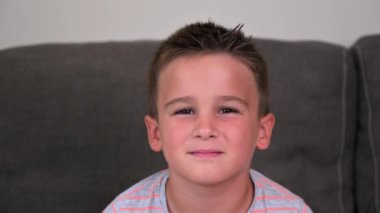 Portrait of a Funny little boy smiling and laughing looking at camera sitting on the couch at home. Concept of a happy childhood. High quality 4k footage