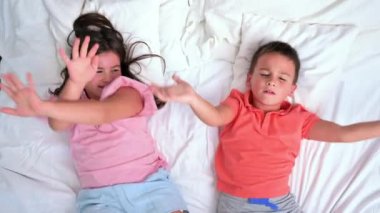 Mutlu kardeşler yatakta uzanıyorlar. Oynuyorlar, eğleniyorlar ve etkileşime giriyorlar. Üst Manzara. Yüksek kalite 4k görüntü