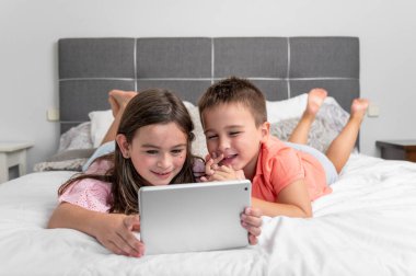 Evde internet kullanan dijital tabletli şirin çocuklar. Kafkasyalı küçük kız ve erkek kardeşler internette sörf yapıyor, yatakta çizgi film izliyorlar. Yüksek kaliteli fotoğrafçılık.