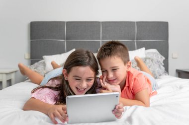 Evde internet kullanan dijital tabletli şirin çocuklar. Kafkasyalı küçük kız ve erkek kardeşler internette sörf yapıyor, yatakta çizgi film izliyorlar. Yüksek kaliteli fotoğrafçılık.