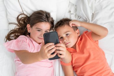 Akıllı telefon kullanan ve evde yatakta yatarken gülümseyen kardeşlerin en iyi görüntüsü. Yüksek kaliteli fotoğrafçılık. Yüksek kalite fotoğraf
