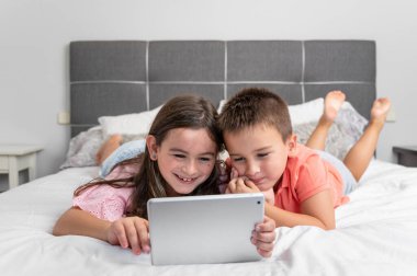 Evde internet kullanan dijital tabletli şirin çocuklar. Kafkasyalı küçük kız ve erkek kardeşler internette sörf yapıyor, yatakta çizgi film izliyorlar. Yüksek kaliteli fotoğrafçılık.