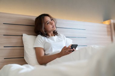 Genç Asyalı kadınlar, geceleri uyuduktan sonra yataktaki akıllı telefonlarda mesajlaşıp sosyal uygulamaları kontrol ediyorlar. Mobil bağımlılık kavramı.