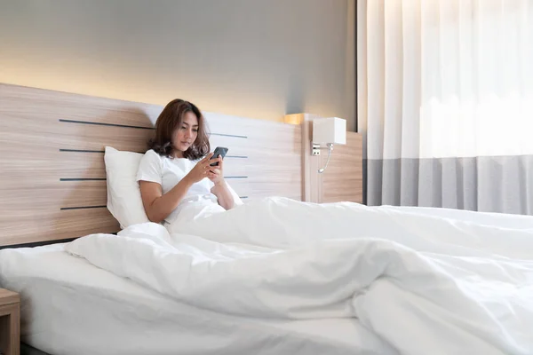 Young asian women lying in bed texting and checking social apps in smartphone on bed before after she sleeping at night. Mobile addict concept.