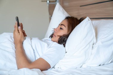 Genç Asyalı kadınlar, geceleri uyuduktan sonra yataktaki akıllı telefonlarda mesajlaşıp sosyal uygulamaları kontrol ediyorlar. Mobil bağımlılık kavramı.