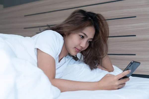 Young asian women lying in bed texting and checking social apps in smartphone on bed before after she sleeping at night. Mobile addict concept.