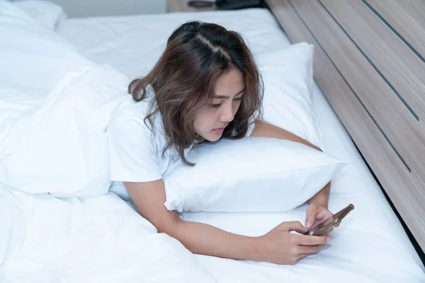 Young asian women lying in bed texting and checking social apps in smartphone on bed before after she sleeping at night. Mobile addict concept.