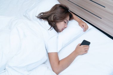 Genç Asyalı kadınlar, geceleri uyuduktan sonra yataktaki akıllı telefonlarda mesajlaşıp sosyal uygulamaları kontrol ediyorlar. Mobil bağımlılık kavramı.