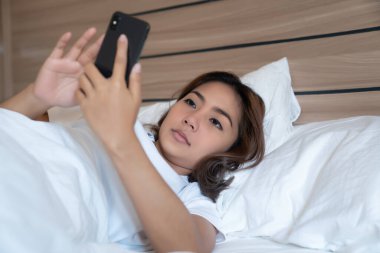 Genç Asyalı kadınlar, geceleri uyuduktan sonra yataktaki akıllı telefonlarda mesajlaşıp sosyal uygulamaları kontrol ediyorlar. Mobil bağımlılık kavramı.