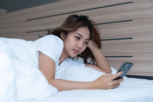 Young asian women lying in bed texting and checking social apps in smartphone on bed before after she sleeping at night. Mobile addict concept.