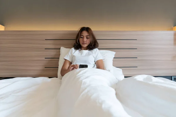 Young asian women lying in bed texting and checking social apps in smartphone on bed before after she sleeping at night. Mobile addict concept.